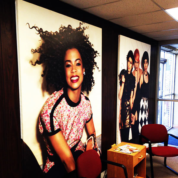 Two large canvas wrapped photographs are displayed against a black wall in a waiting area. They feature young women in stylish clothing.