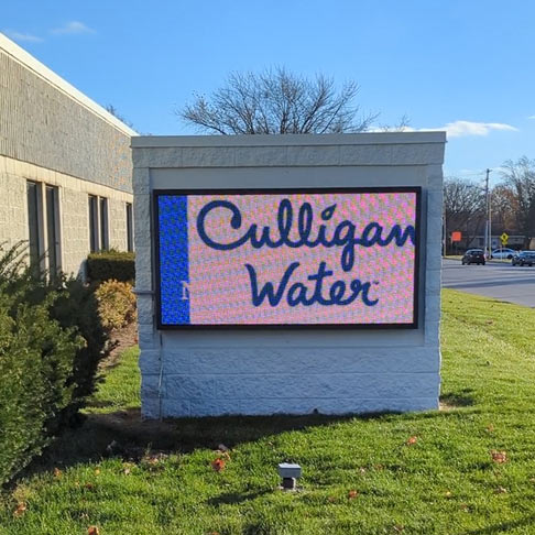 A digital sign for Culligan Water in the green grass outside of an office building.