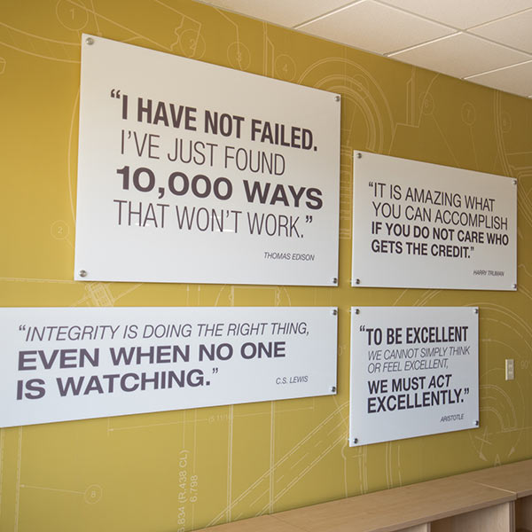 Various motivational quotes on printed on whiteboards and mounted against a mustard yellow wall.