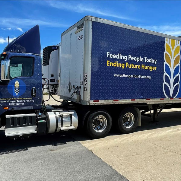 A company logo for "Hunger Task Force" on the side of a semi truck. It reads "Feeding People Today Ending Future Hunger. Www.hungertaksforce.org."