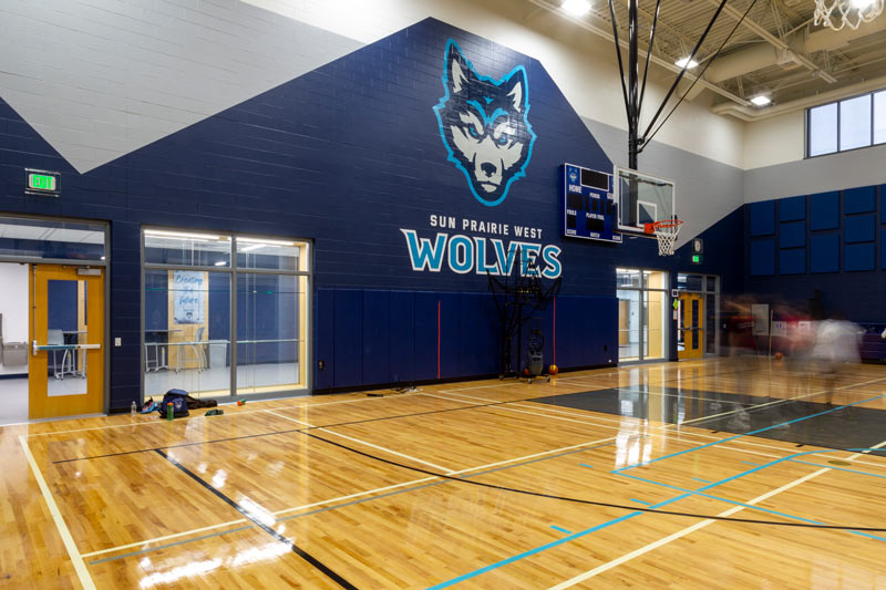 A wolf mascot is featured against the wall of an indoor basketball arena.