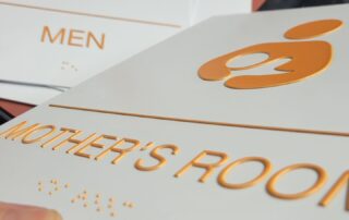 A hand holding a "mother's room" sign with a men's room sign in the background.